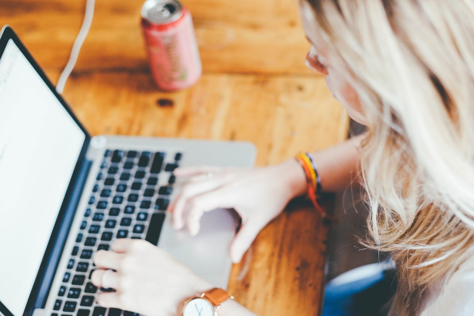 overhead view of woman typing on laptop with can of soda nearby