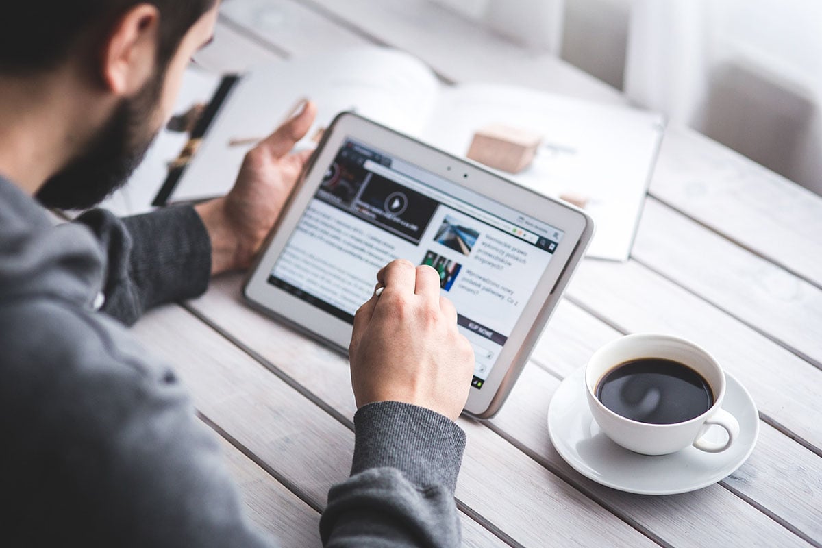 man looking at website on tablet with coffee and books nearby