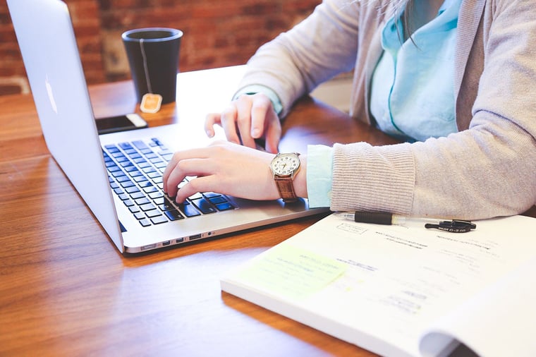 woman typing on laptop with open textbook and tea and tea
